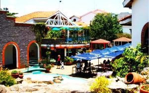 A vibrant outdoor courtyard with greenery, seating areas under umbrellas, and a charming building in Kenya.