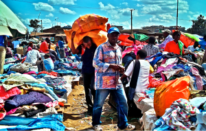 Shoppers browsing through piles of second-hand clothes at a vibrant open-air market in Nairobi, Kenya.