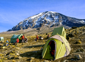 a group of people camping in a rocky area with mountain Kilimanjaro in the background - a great way to experience combined safaris in Tanzania and Kenya